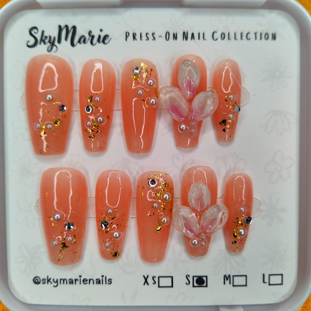 SkyMarie small peach press-on nails with 3D floral petals, pearls, and glitter.