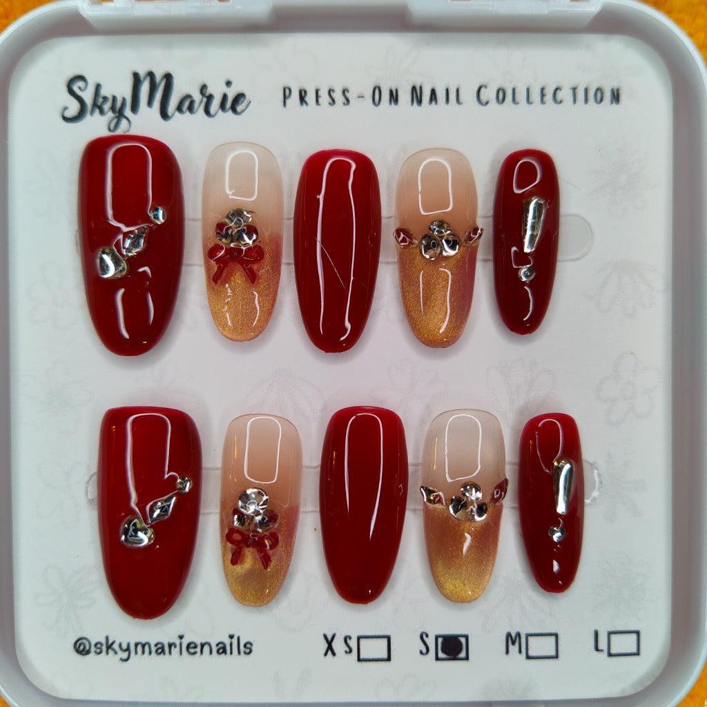 SkyMarie small press-on nails: red & gold gradient with rhinestones, silver bows, and solid red accents.