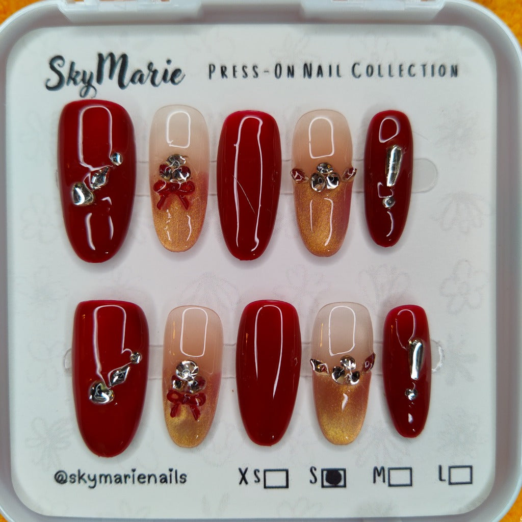 SkyMarie small press-on nails: red & gold gradient with rhinestones, silver bows, and solid red accents.