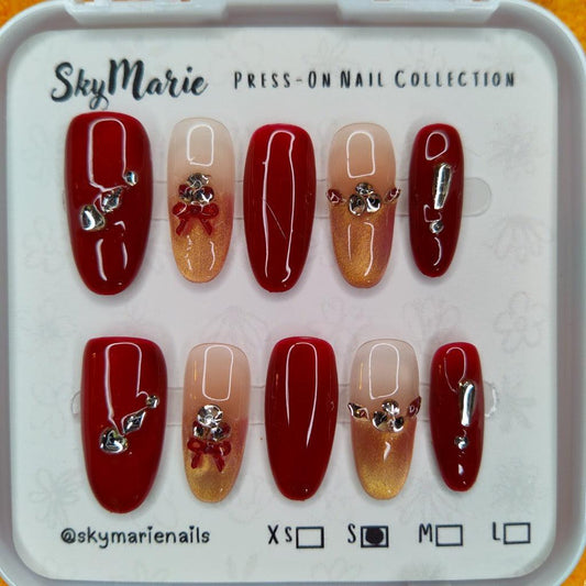 SkyMarie small press-on nails: red & gold gradient with rhinestones, silver bows, and solid red accents.