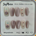 SkyMarie small press-on nails: shimmering mauve cat eye and milky-white with pink floral designs & rhinestones.