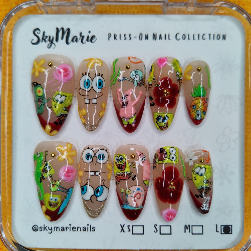 SkyMarie large Spongebob press-on nails with cartoon characters, clear-to-red ombre, and gold studs.