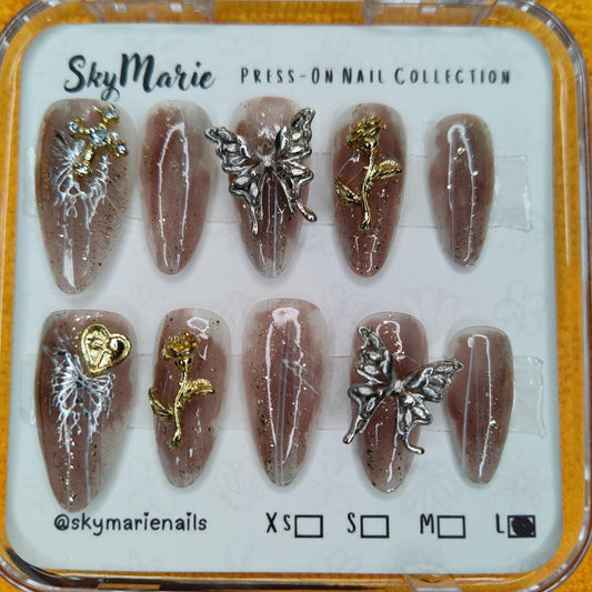Brown ombre glitter press-on nails with silver butterflies, gold roses, and a gold heart charm.