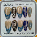 SkyMarie large press-on nails: blue french tips with rhinestones, gold chrome, and abstract blue designs.